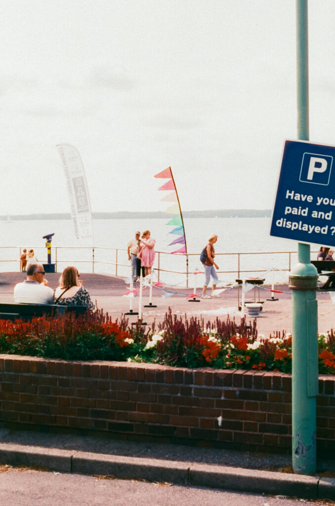 An image of people on the edge of a path by the see with a set of flags next to them