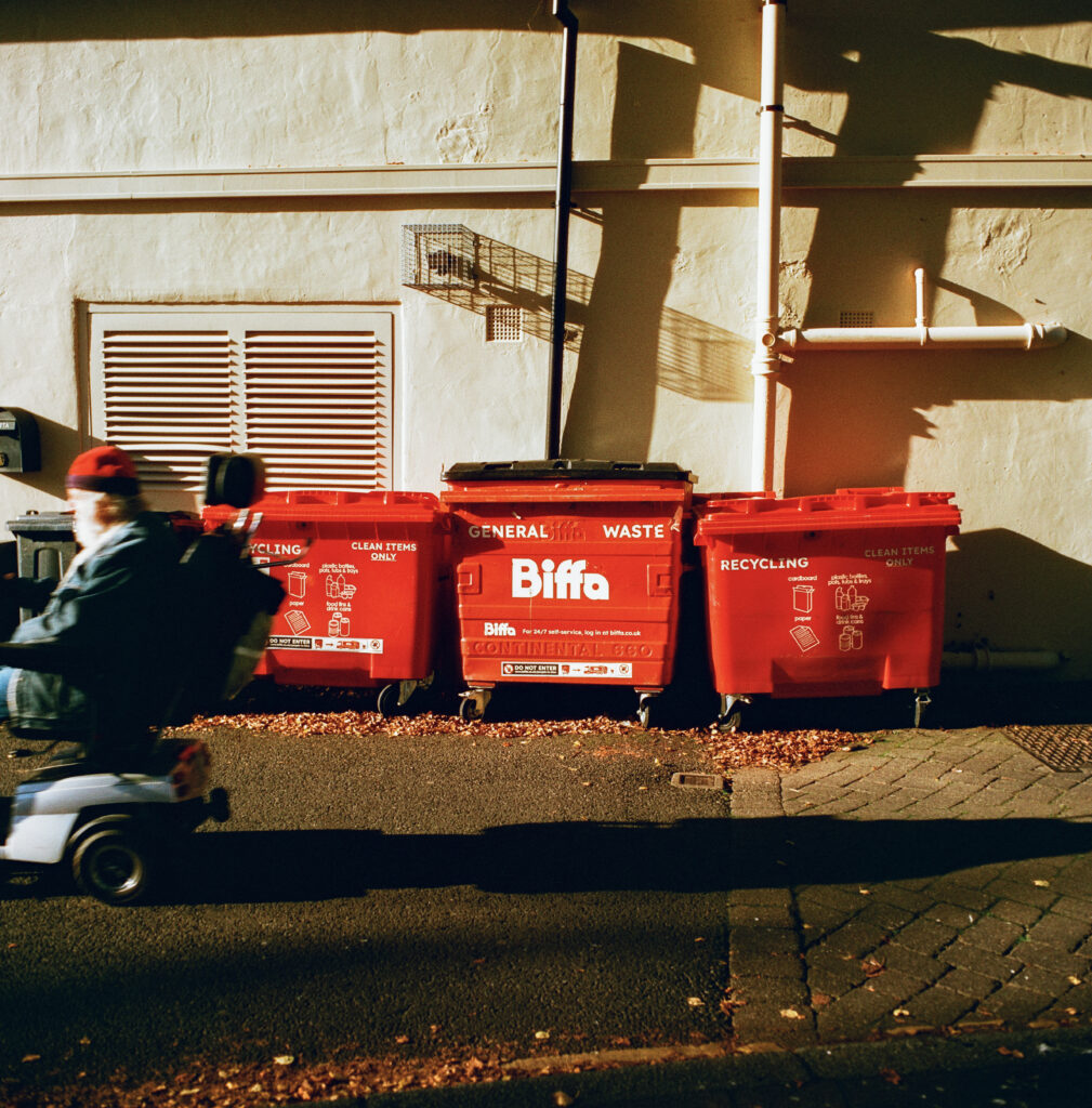 A row of Biffa bins with a man riding a moped past the frame