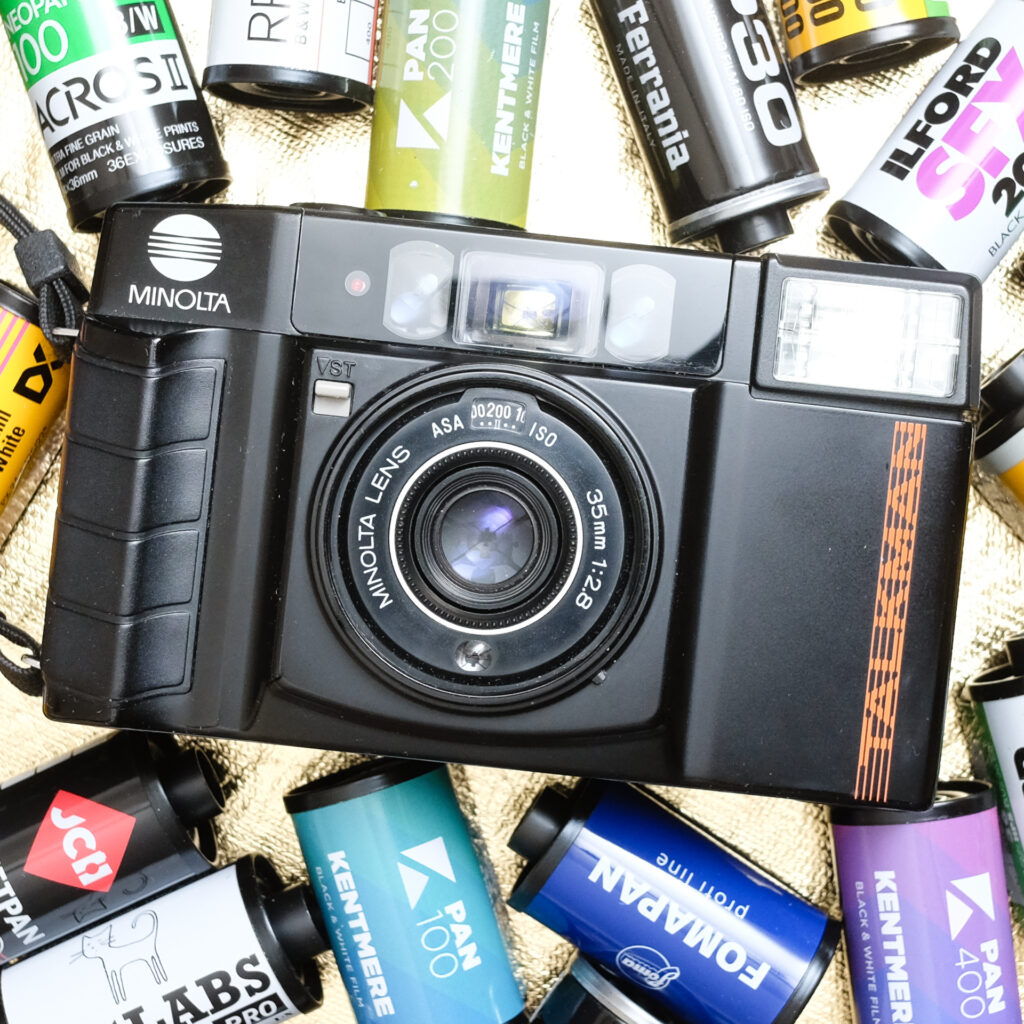 Front view of a Minolta Talkman camera surrounded by 35mm film cassettes