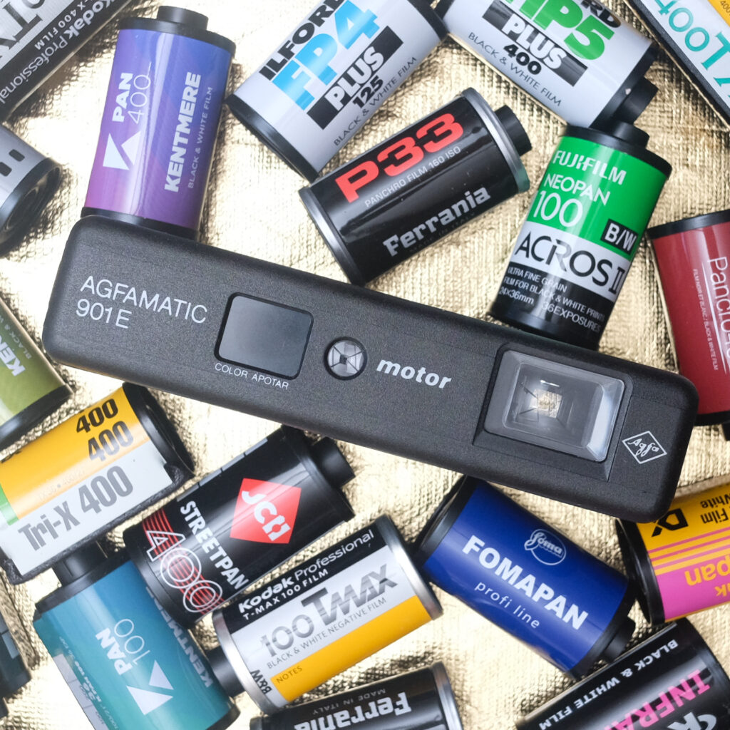 Front view of an Agfa Agfamatic 901 E Motor camera surrounded my 35mm film cassettes